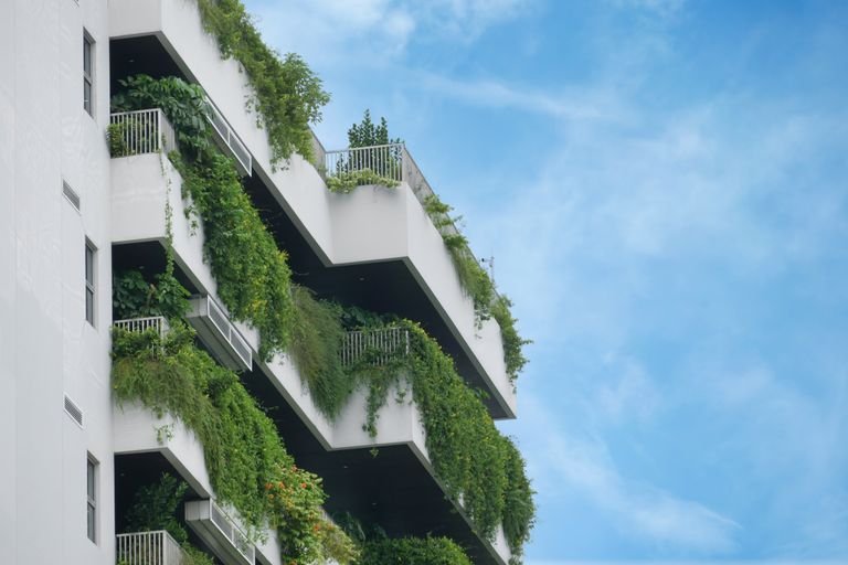 A residential building showcasing lush vertical gardens on multiple balconies against a clear blue sky.