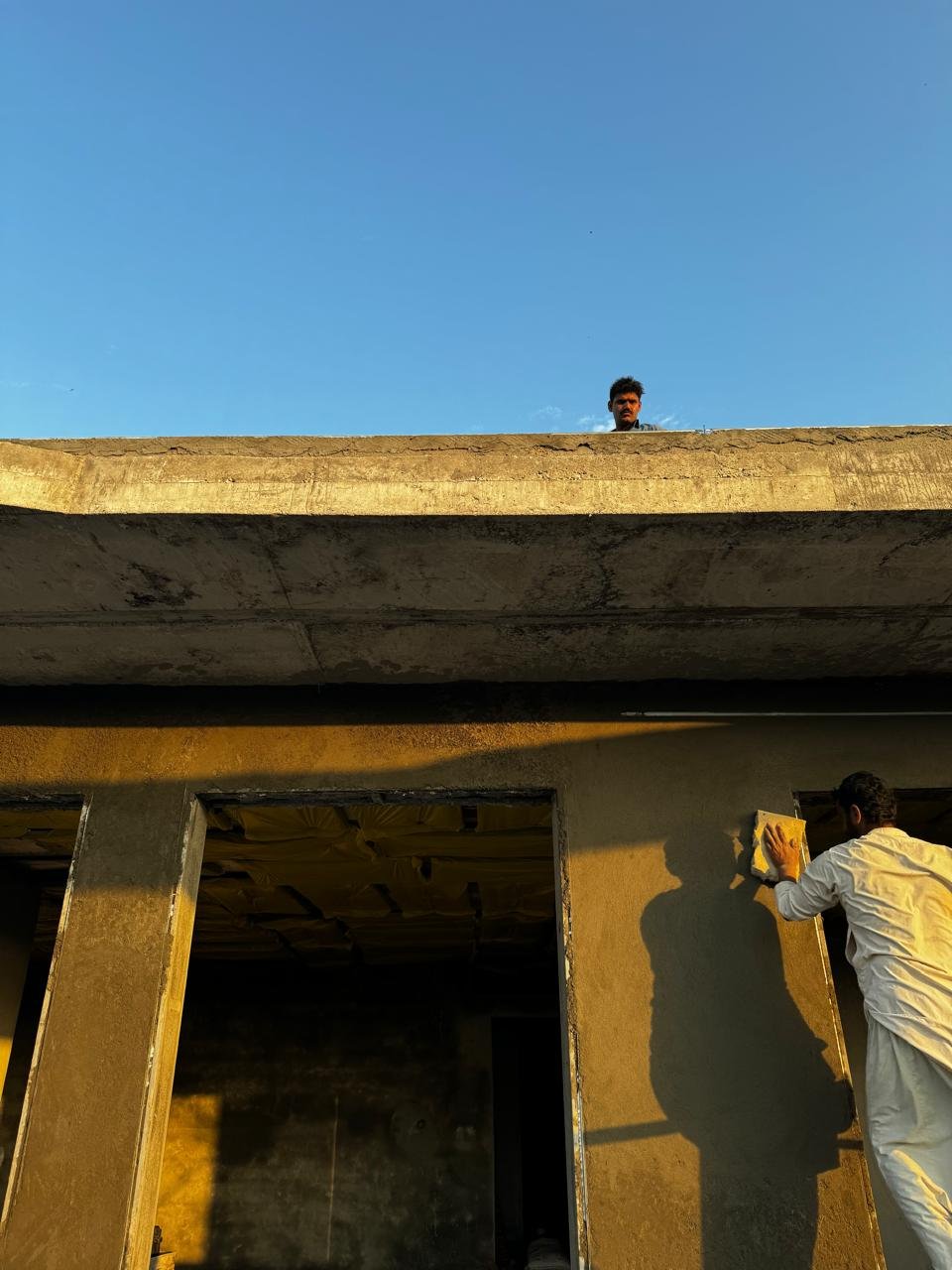 Worker applying exterior render beneath a concrete roof edge against a blue sky.