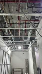 Exposed pipework, ventilation ducts, electrical wiring and metal ceiling framing before the suspended ceiling is closed.