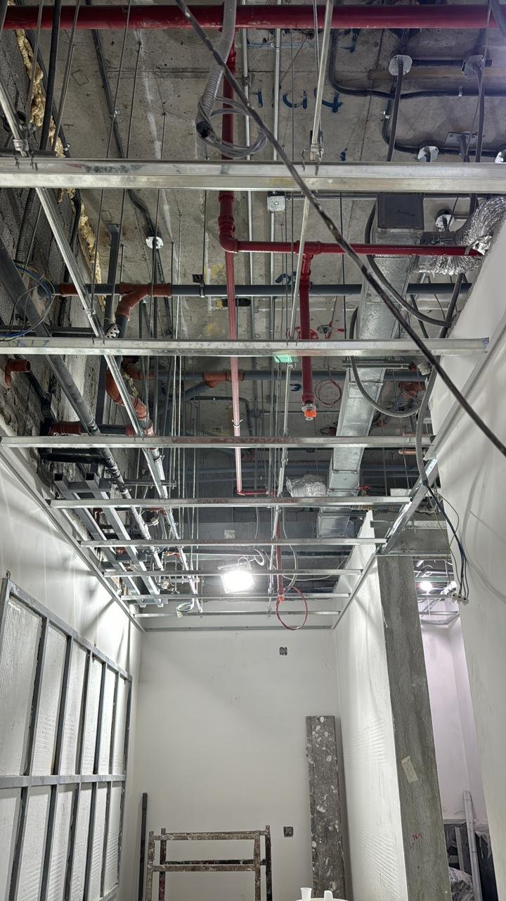 Exposed pipework, ventilation ducts, electrical wiring and metal ceiling framing before the suspended ceiling is closed.